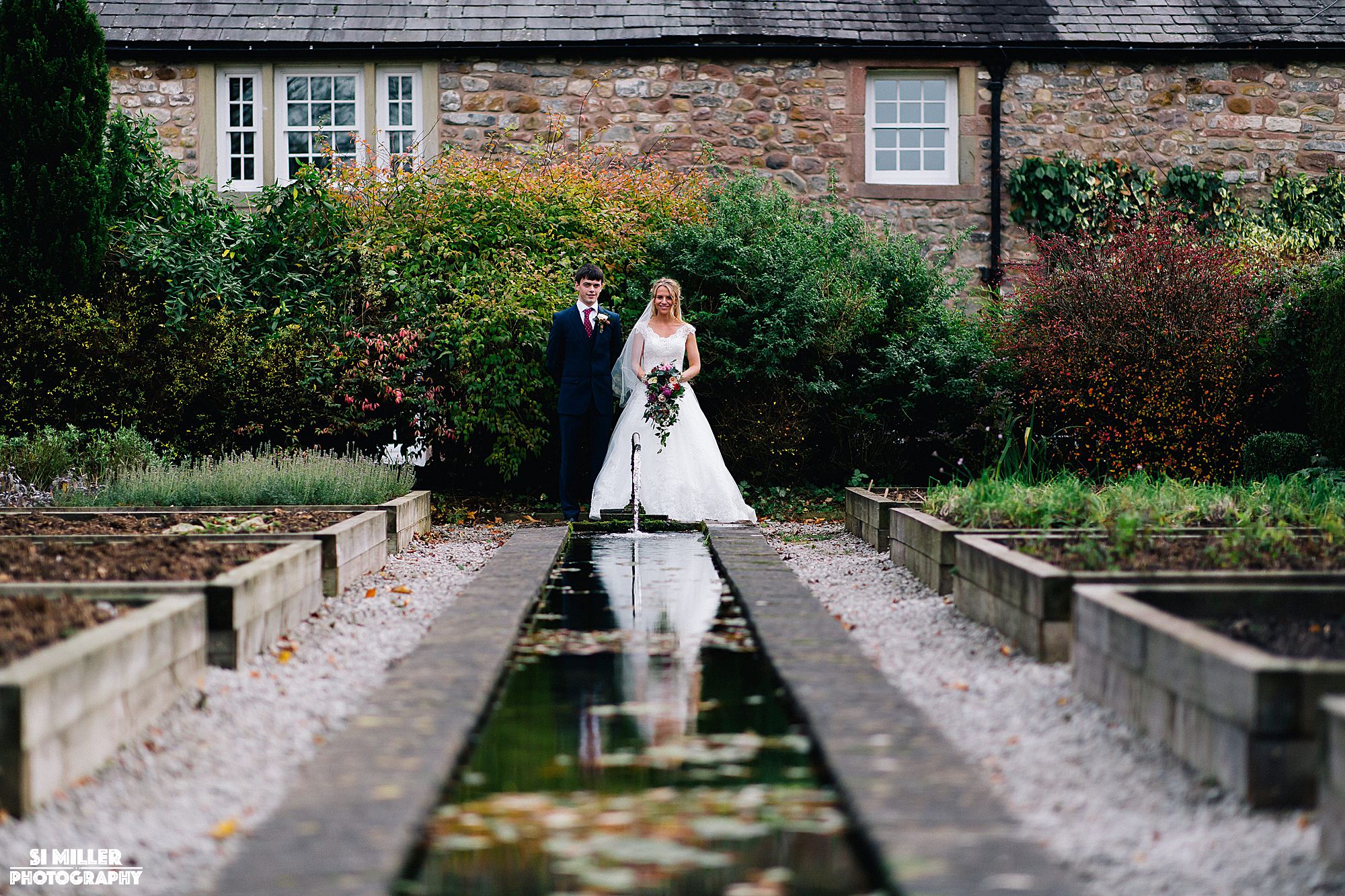 Bride and groom in gardens at inn at Whitewell with reflection in water